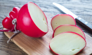 Cheese, wrapped in a red wax coating, is sliced and displayed on a cutting board.